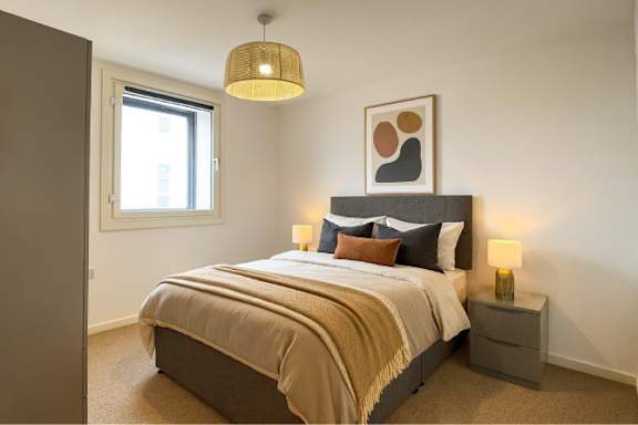 A bedroom with a large bed and a lamp on the side table.
