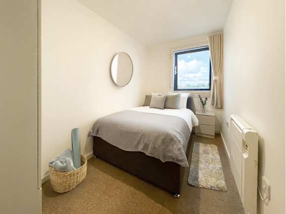 A bedroom with a bed, a window, and a basket on the floor.