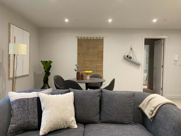 A grey couch with a white pillow and a grey hat on it.