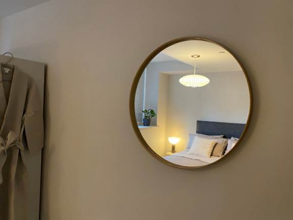 A round mirror hangs on a wall above a bed.