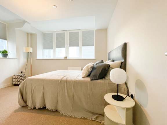 A bedroom with a bed, a side table, and a window.