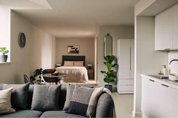 A modern living room with a grey couch and a white kitchen in the background.