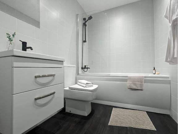 A white bathroom with a towel on the bathtub.