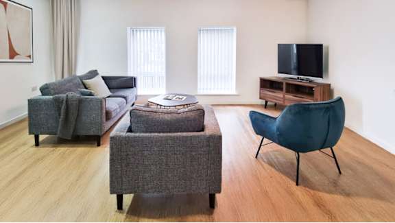 A living room with a grey couch, a grey ottoman, a blue chair and a television.