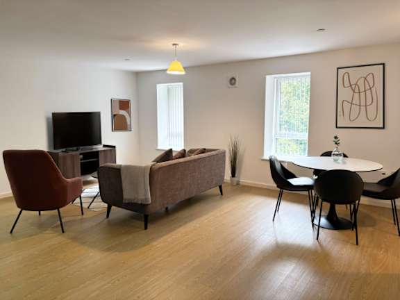 A living room with a brown couch, a red chair, a black chair, and a round table.