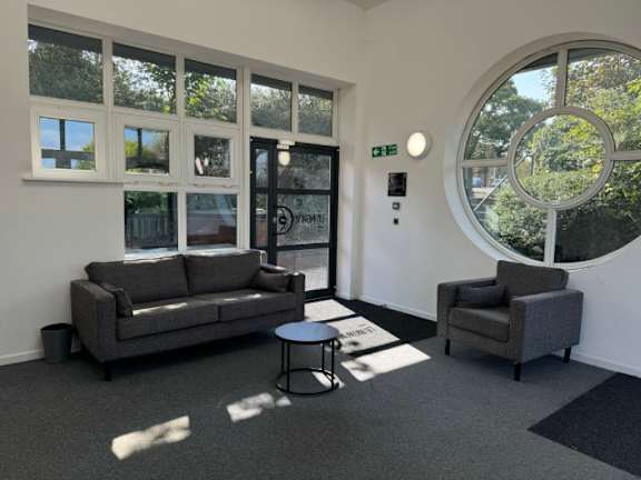 A grey couch and chair are placed in a room with a large window and a round window.
