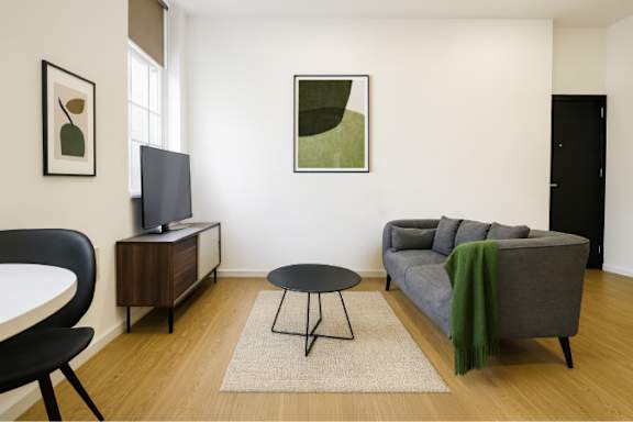 A living room with a grey couch, a black chair, a small table, and a television.