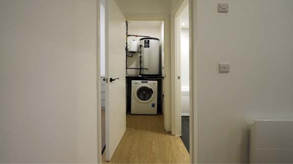 A white washing machine is in a narrow hallway.