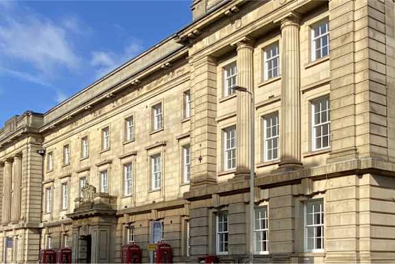A large, beige-colored building with many windows and a statue on the left side.
