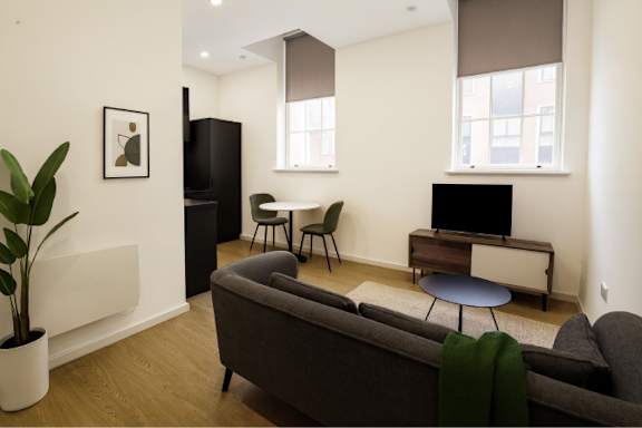 A living room with a grey couch and a black fridge.