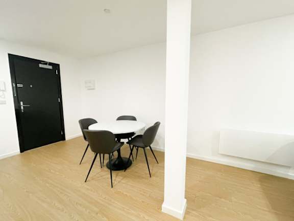 A black door is on the left of a white wall with a table and chairs in the middle of the room.