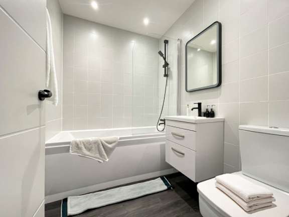 A white bathroom with a white tub, white towel, and white toilet.