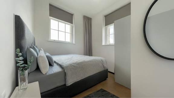 A bedroom with a bed, a vase with plants, and a round mirror on the wall.