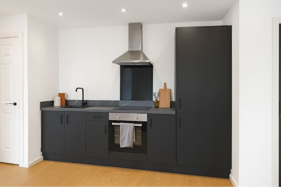 A modern kitchen with black cabinets and a stainless steel range hood.