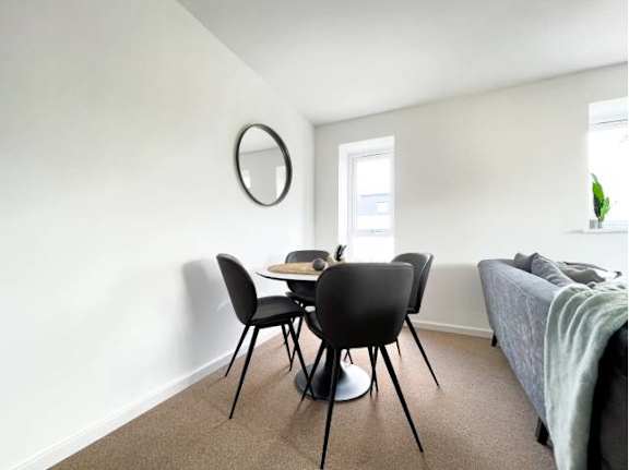 A round mirror hangs on a white wall above a black table and four chairs.