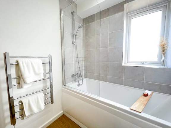 A bathroom with a white tub, a towel rack with white towels, and a window.