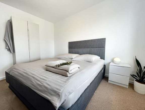 A bedroom with a bed, nightstand, and a plant.