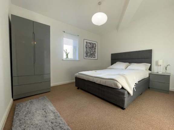 A bedroom with a bed, nightstand, and a grey rug.