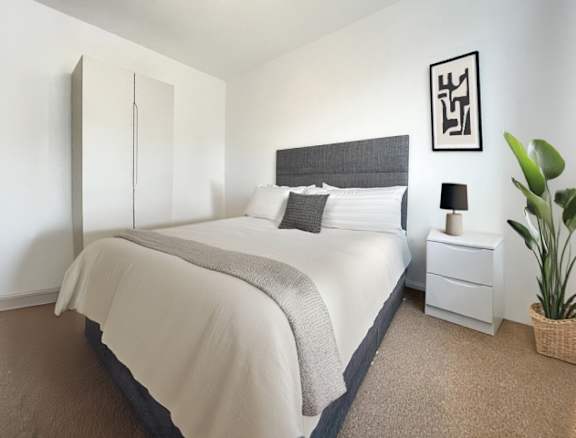 A bedroom with a large bed and a plant on the side table.