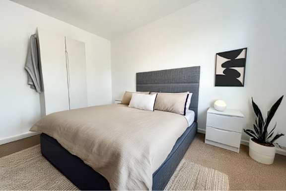 A bedroom with a bed, nightstand, and a plant.