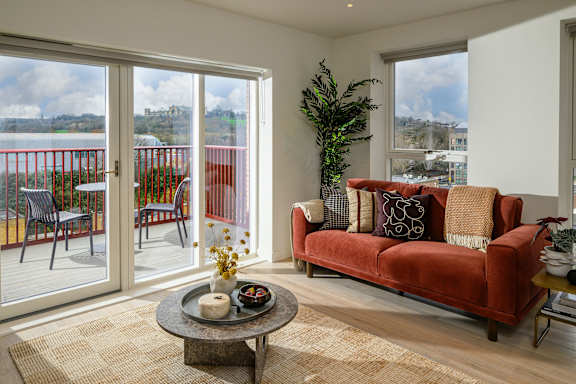 A living room with a red couch and a glass door leading to a balcony.