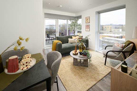 A living room with a grey sofa, a grey armchair, a coffee table, and a table with a vase of flowers and cups on it.