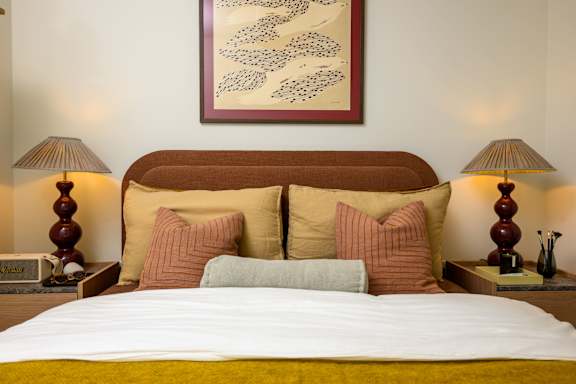 A bed with a white comforter and a yellow blanket is flanked by two lamps on either side.