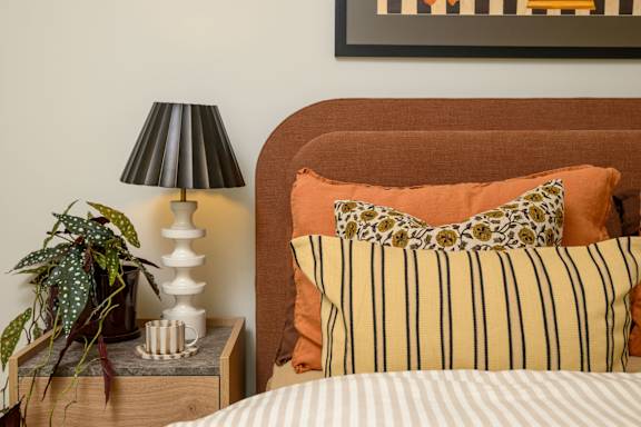 A bedroom with a bed, a lamp, and a potted plant.