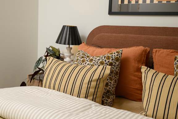 A bed with striped pillows and a leopard print pillow is in front of a brown headboard.