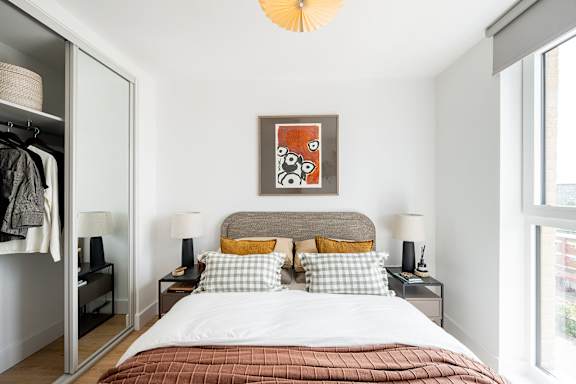 A bedroom with a bed, two lamps, a painting, and a wardrobe.
