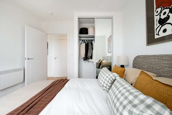 A bedroom with a large bed and a closet with clothes hanging inside.