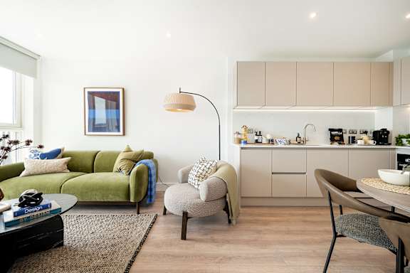 A modern living room with a green couch and a kitchen area in the background.