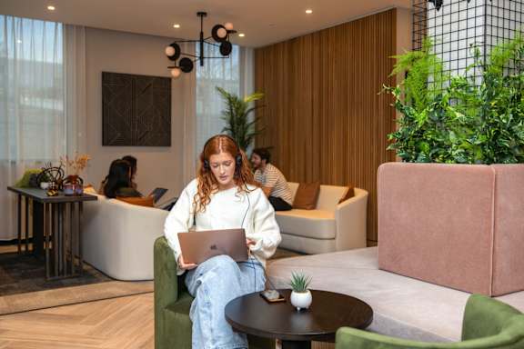 A woman with a laptop sits on a green couch in a modern room.