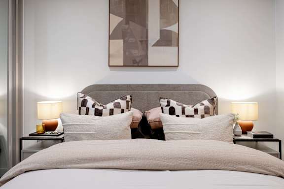 A bed with a grey headboard and two pillows with a checkered pattern.