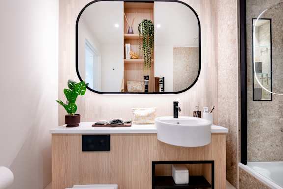 A bathroom with a round mirror, a sink, and a plant.