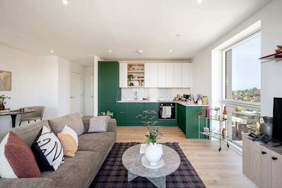 A living room with a grey couch and a coffee table in front of a green kitchen.