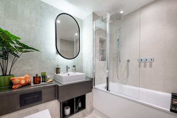 A modern bathroom with a white bathtub and a round mirror above a sink.