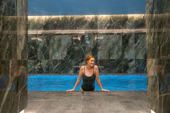 A person swims in a pool in a modern, marble-adorned room.