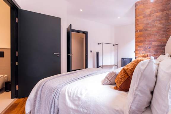 A bedroom with a bed, pillows, and a brick wall.