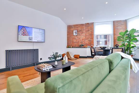 A living room with a green couch and a flat screen TV mounted on the wall.