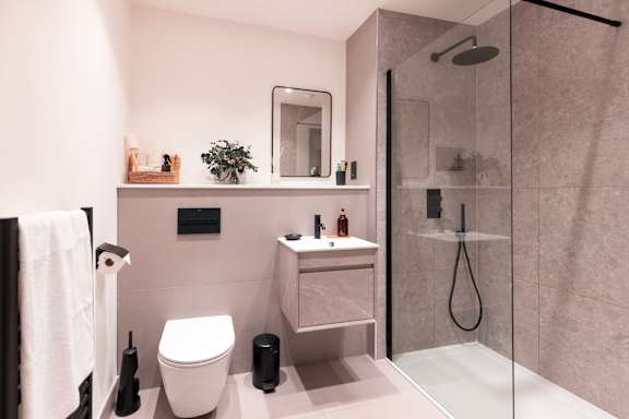 A bathroom with a toilet, sink, mirror, and shower.