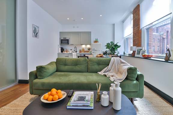 A green couch with a bowl of oranges on a coffee table in a modern kitchen.