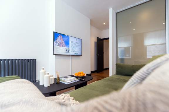 A living room with a couch, a table with bottles and a book, and a TV screen showing a building.
