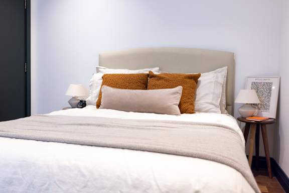 A bed with a white comforter and two pillows with orange throw pillows on top.