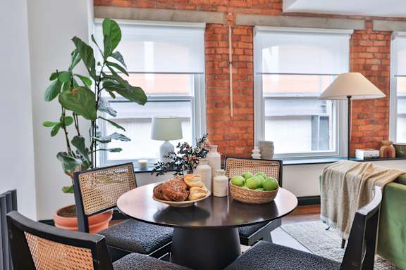 A dining table with chairs and a potted plant in a room with a brick wall.