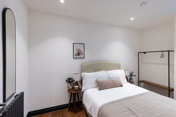 A bedroom with a large bed and a small table with a vase and plant on it.