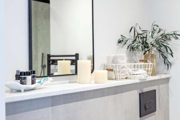 A bathroom counter with a mirror, candles, and a plant.