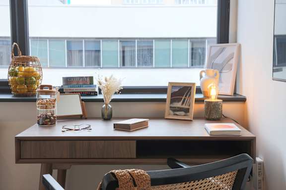 A desk with a chair and a window with a view of a building.