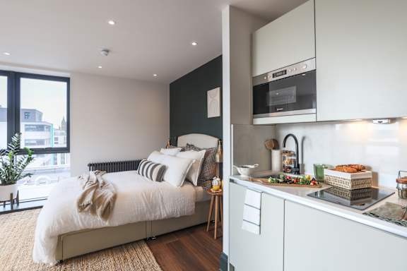 A bedroom with a bed and a kitchen area in a house.