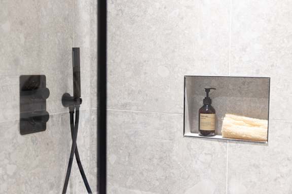 A bottle of soap is on a shelf in a bathroom.